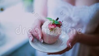 在茶托上近距离观看漂亮的纸杯蛋糕。 女人拿着一盘蛋糕，闻着甜点的味道。